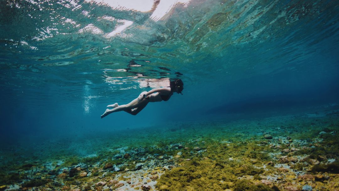 Woman snorkeling in crystal-clear turquoise waters above a rocky reef in Tulum, perfect for a complete 2026 snorkeling guide.