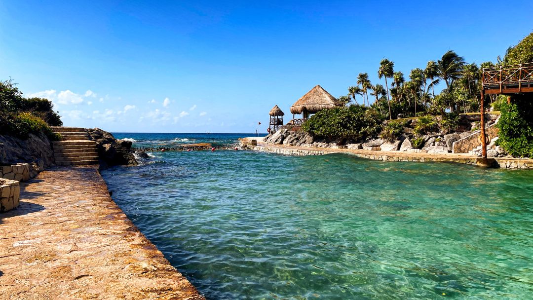 Turquoise coastal lagoon with stone walkway, palapa huts, and palm trees in Tulum, ideal for a 3-day itinerary for first-time visitors.